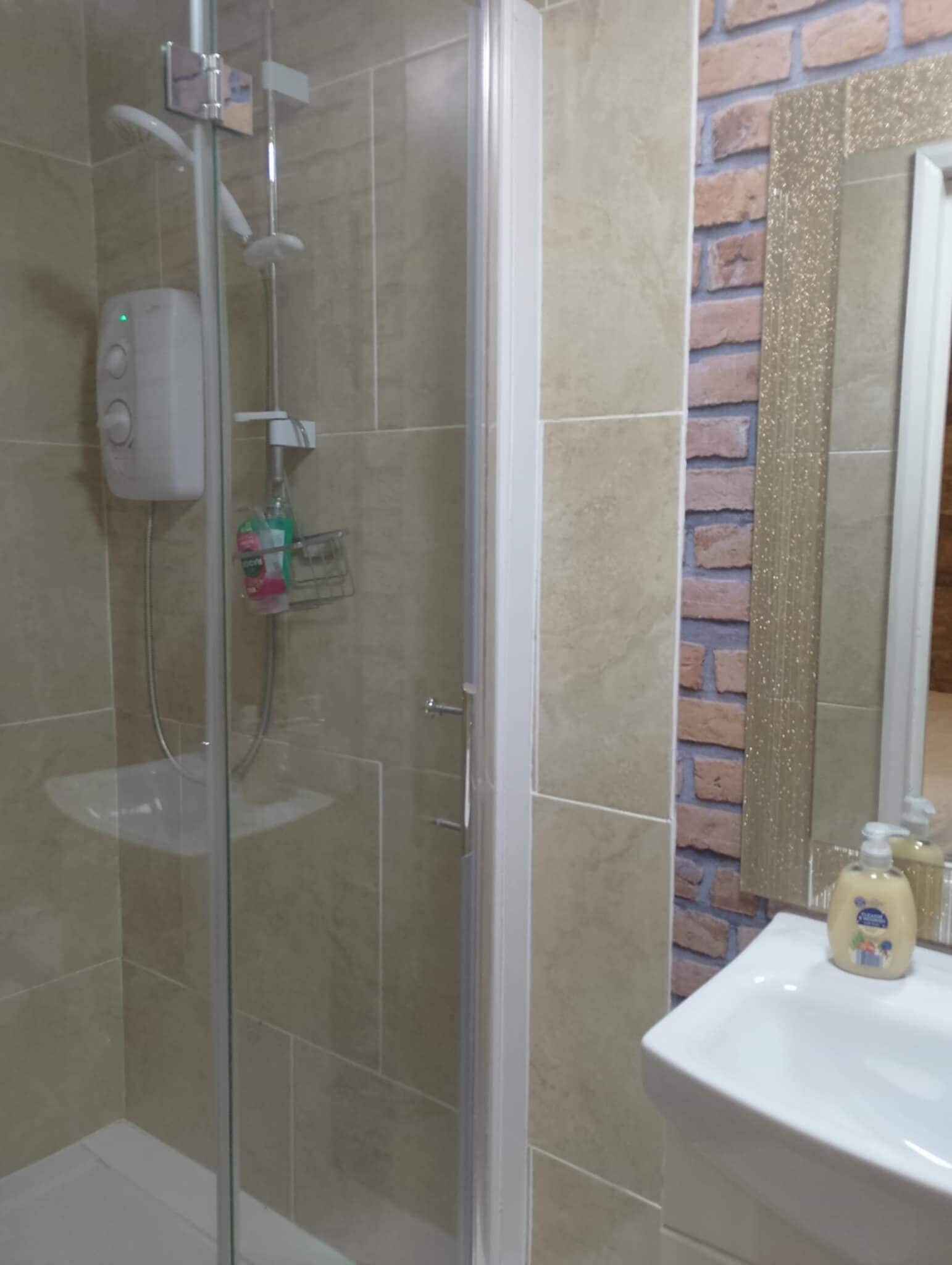 A bathroom with a glass-enclosed shower, a white sink, and a mirror with a brick wall design.