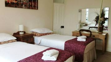 Ein Hotelzimmer mit zwei Betten, einem Schreibtisch, einem Stuhl, einem Spiegel und einem Bild an der Wand.