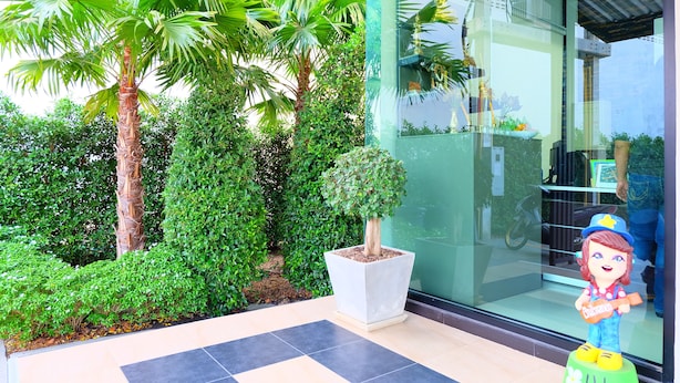 A well-maintained garden with palm trees and a potted plant in front of a building with a glass entrance. - Nai-Ya-Place (Kanchanaburi)