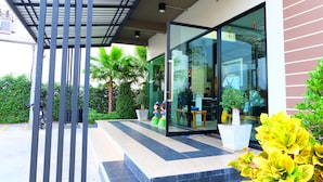 A modern building entrance with a glass door, a covered outdoor area with metal railings, and potted plants. - Nai-Ya-Place (Kanchanaburi)