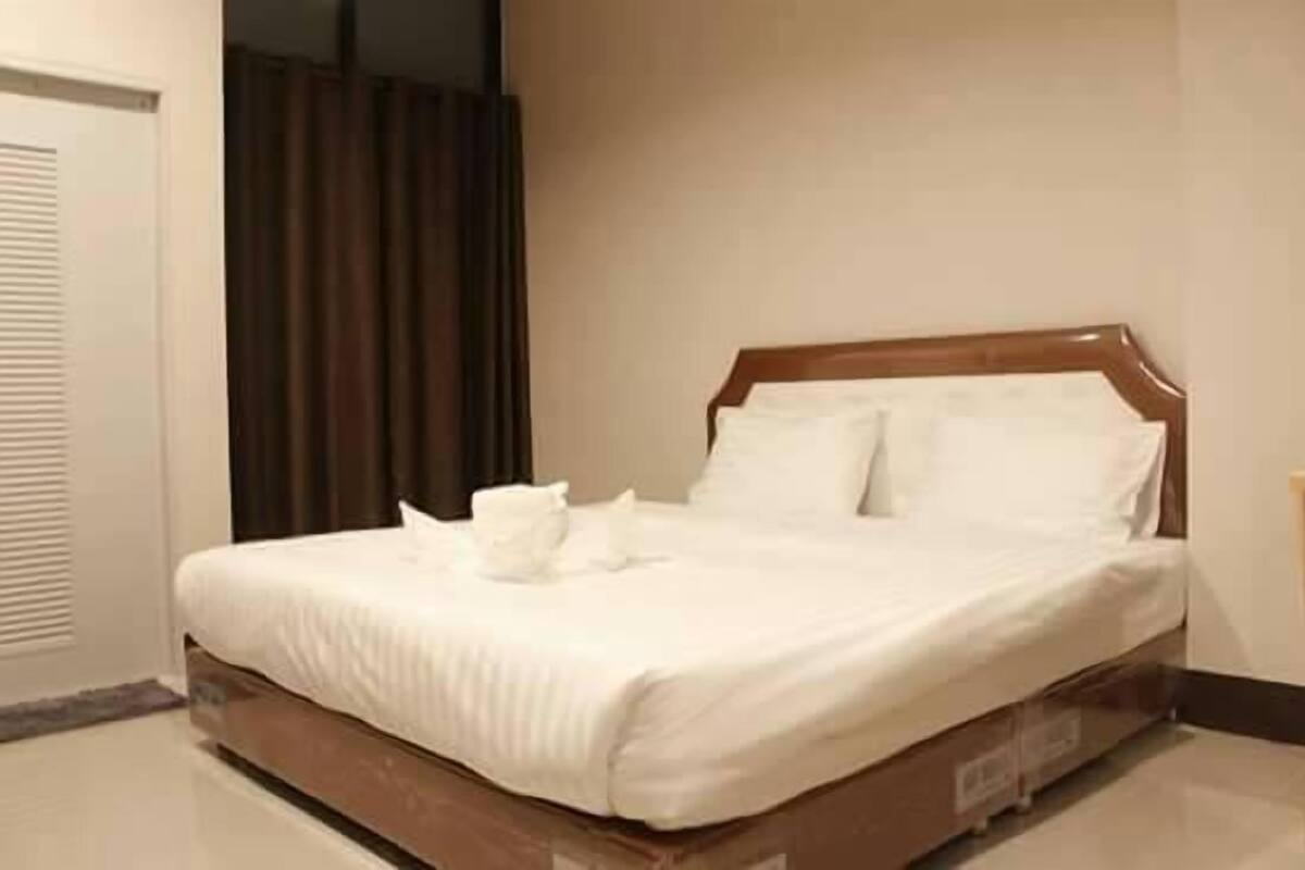 A neatly made bed with white linens and pillows, a wooden headboard, and a brown floor.