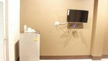 Una habitación con televisión de pared, un refrigerador pequeño y una puerta blanca.