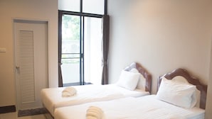 A hotel room with two single beds, a window with curtains, and a door with a louvered design. - Nai-Ya-Place (Kanchanaburi)