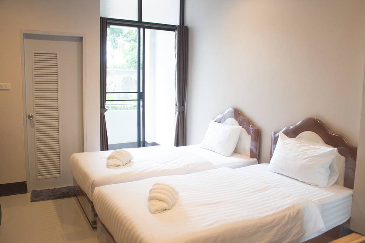A hotel room with two single beds, a window with curtains, and a door with a louvered design.