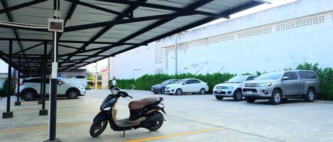 Un estacionamiento con una sección techada, una moto y varios coches.