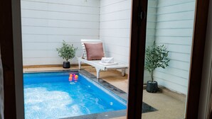 Pequena piscina interior com uma espreguiçadeira branca e duas plantas em vasos.