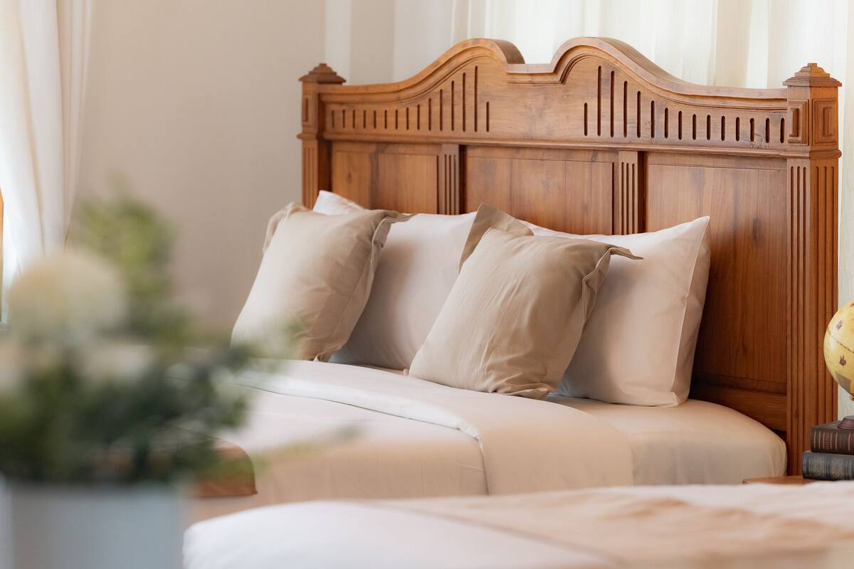 A bedroom with a wooden headboard, a bed with beige bedding, and a bedside table with books.