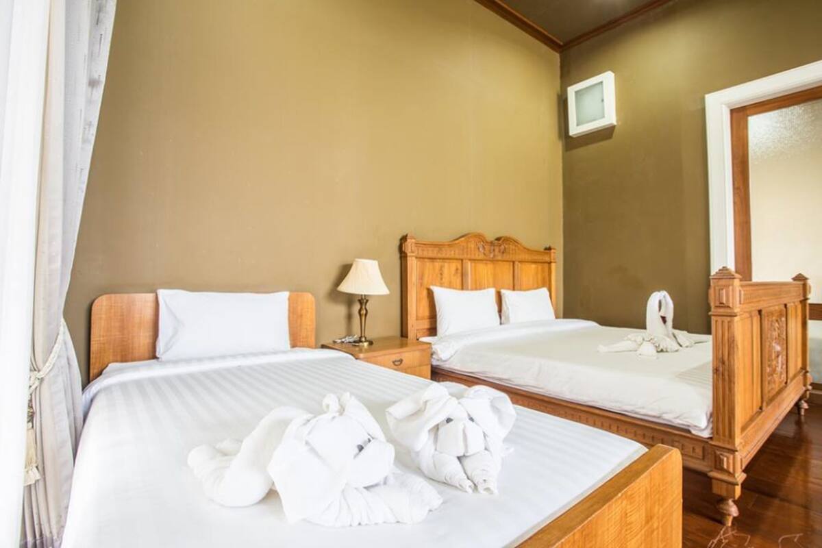 A hotel room with two beds, wooden headboards, white linens, and a large mirror.