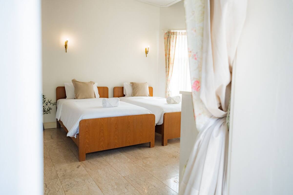 A hotel room with two wooden beds, white linens, and a floral curtain.