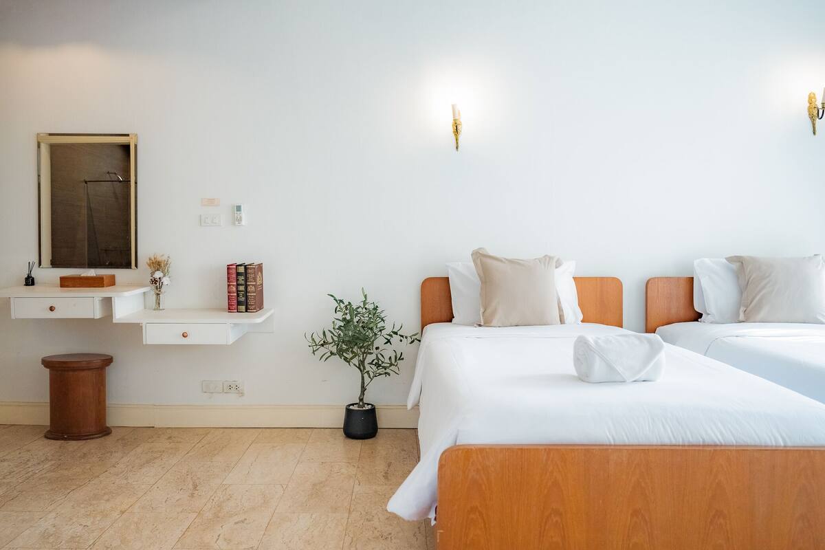 A hotel room with two beds, a small desk, a mirror, and a potted plant.