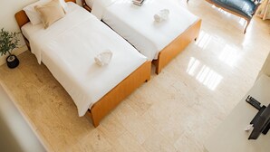 Quarto de hotel moderno com duas camas, um candelabro, um sofá e uma planta em vaso.