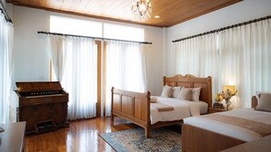 Um quarto com uma cama de madeira, um piano e uma janela grande com cortinas.