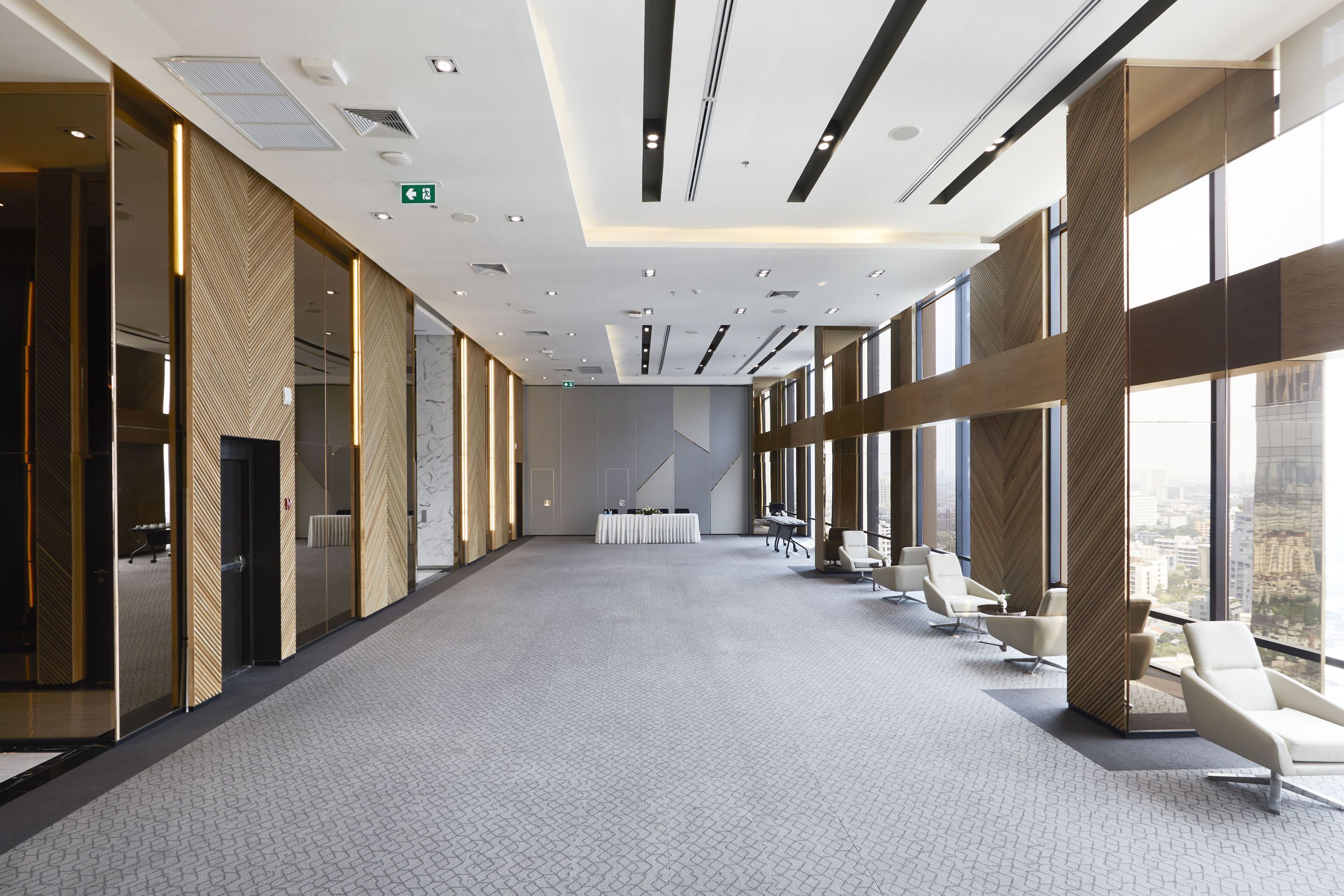 Una sala de conferències àmplia i moderna amb una taula llarga i cadires blanques, grans finestres que ofereixen vista a la ciutat i una moqueta amb dibuixos.