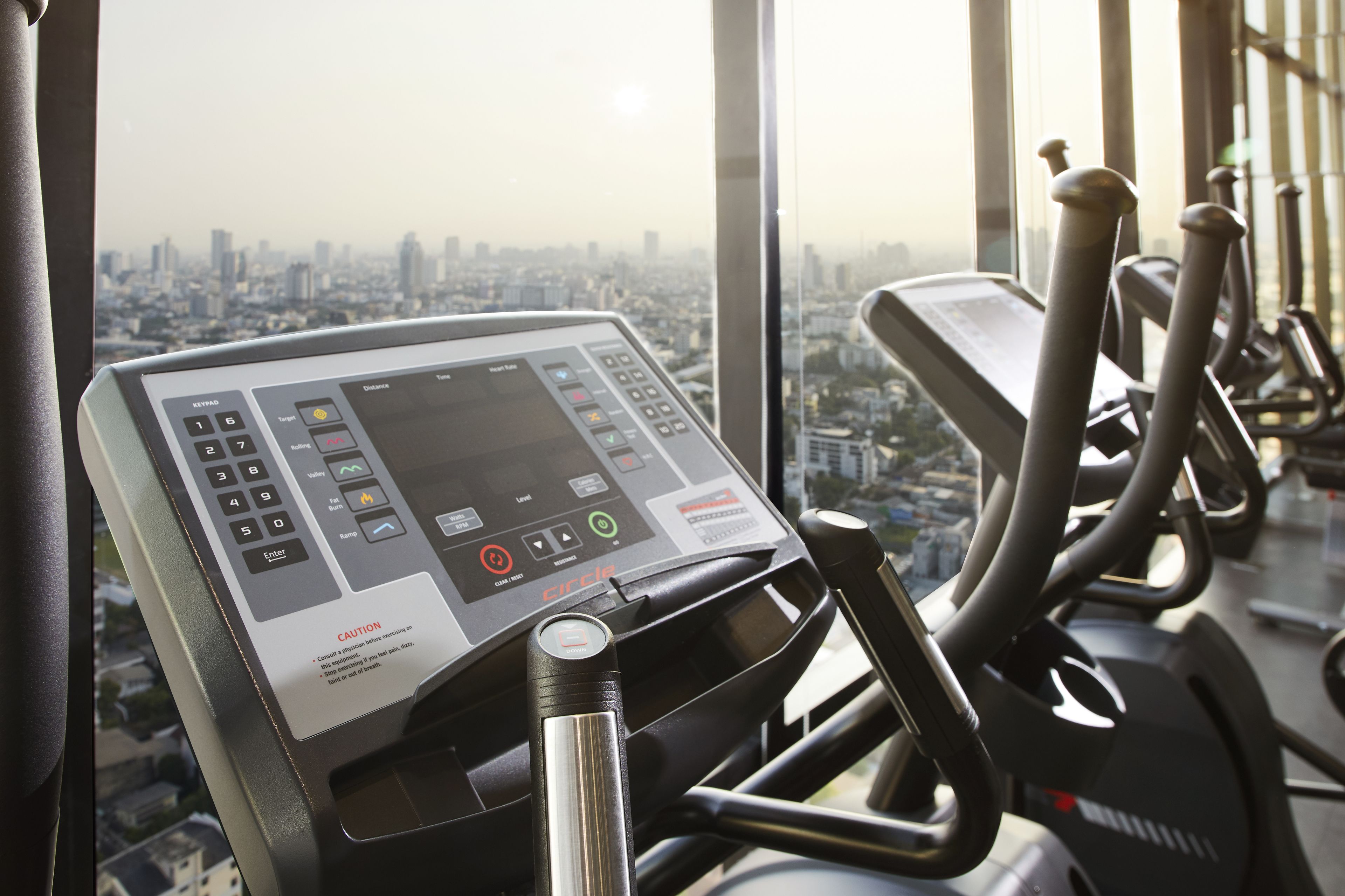 A gym with a treadmill and a control panel with a city view.