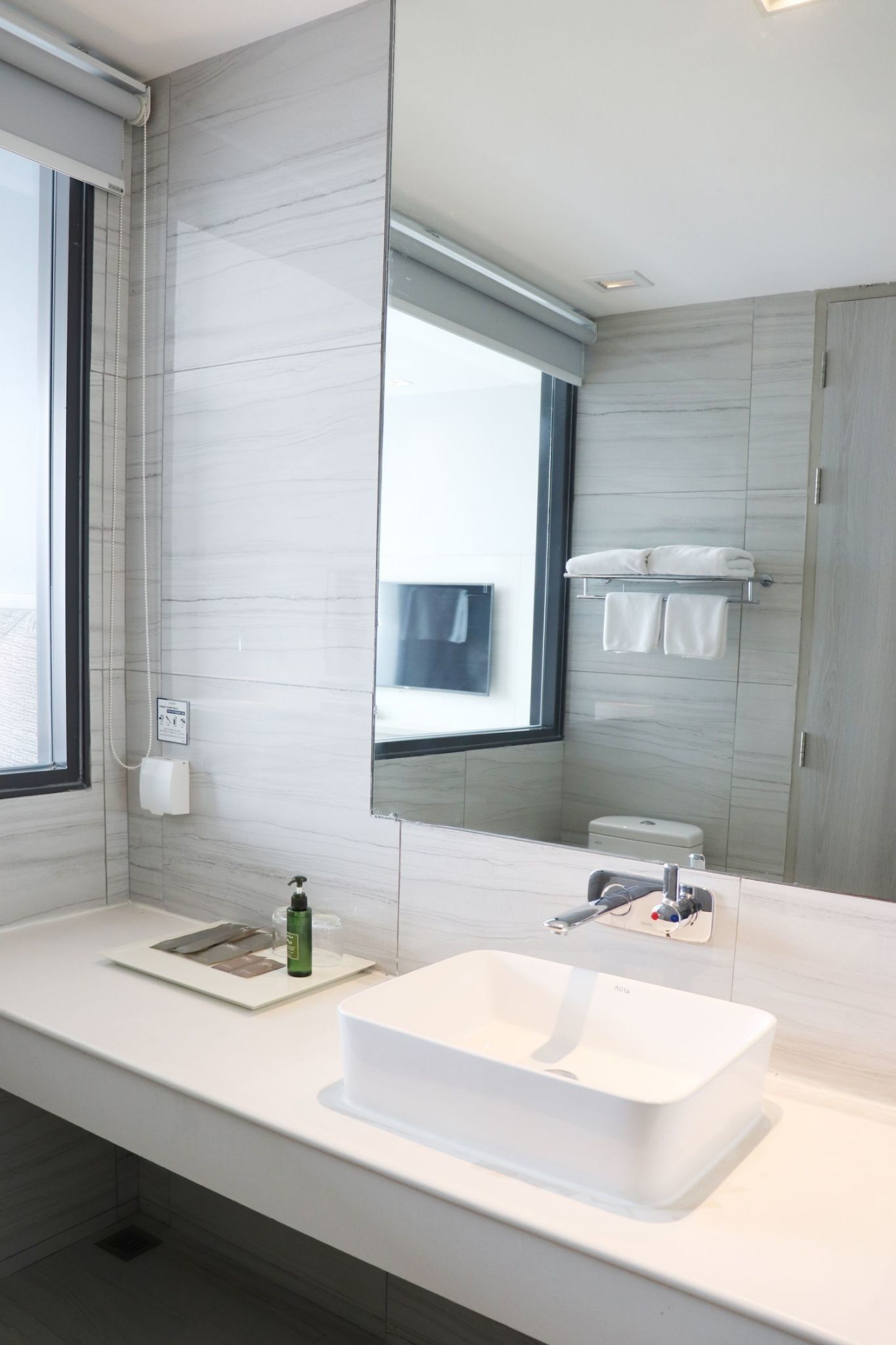 Een moderne badkamer met een grote spiegel, een witte wastafel en een handdoekhouder.