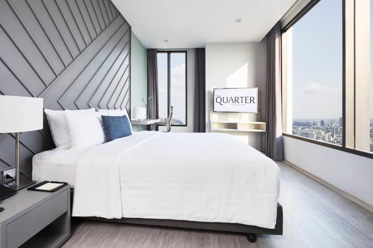 Ein modernes Hotelzimmer mit einem großen Bett, einem Schreibtisch mit Lampe, einem Fernseher und Blick auf die Stadt.