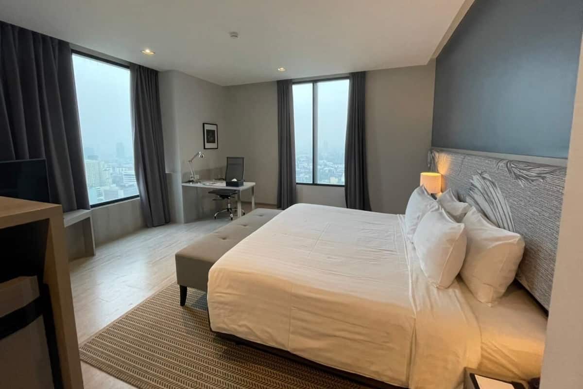 Ein modernes Hotelzimmer mit einem großen Bett, einem Schreibtisch und Blick auf die Stadt.