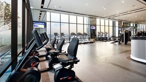 Un gimnasio moderno con equipo de cardio, máquinas de pesas y un amplio ventanal con vista a la ciudad.