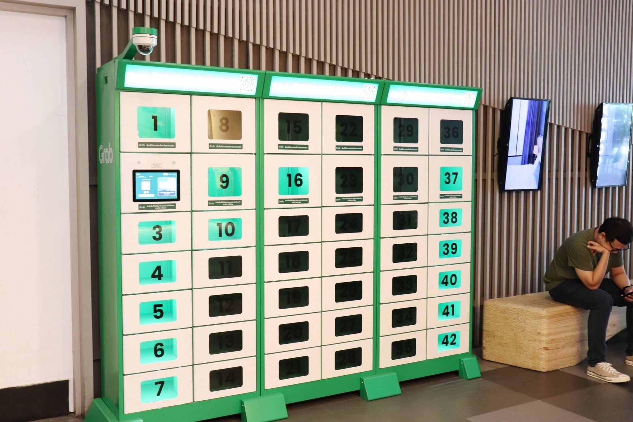 Fila de taquillas numeradas en un espacio público, con una cámara de seguridad arriba y una pantalla de televisión a la derecha.