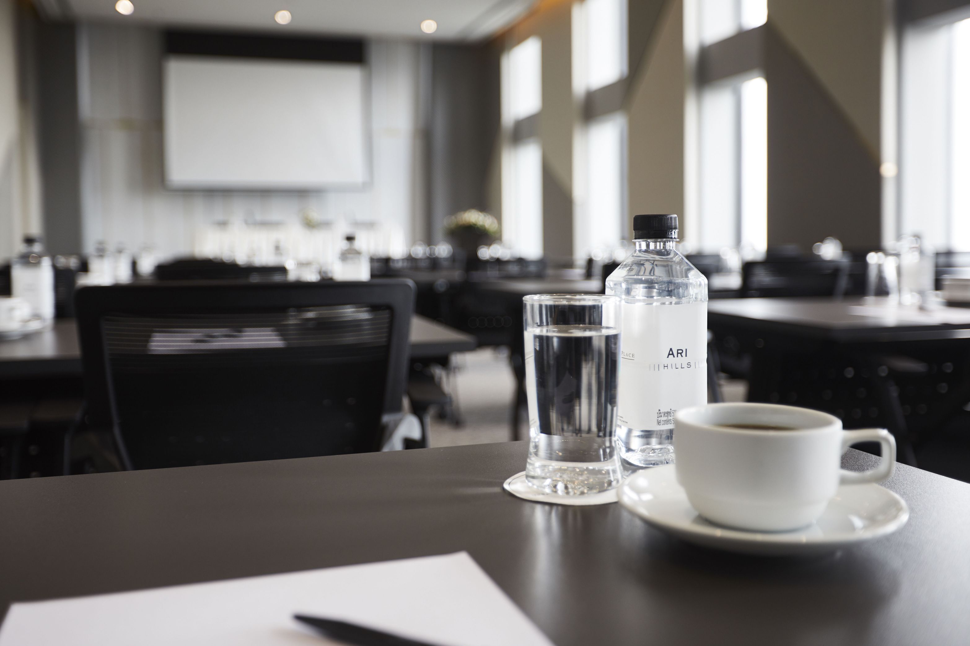 A dining table with a water bottle, a glass, and a cup of coffee in a modern restaurant setting.