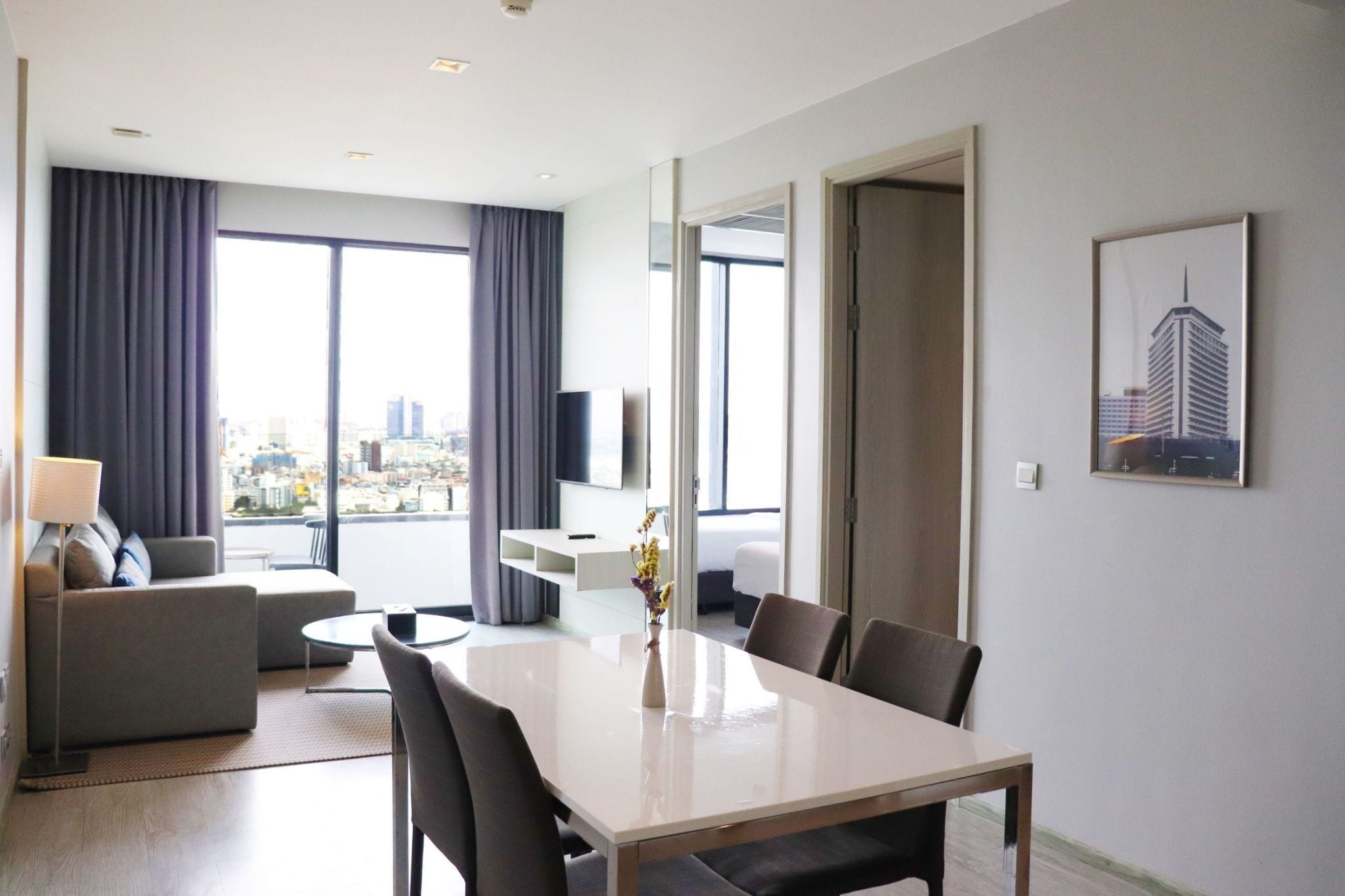 A modern hotel room with a dining area, a sofa, a TV, and a city view.