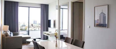 Habitación de hotel moderna con zona de comedor, sofá, televisor y vistas a la ciudad.