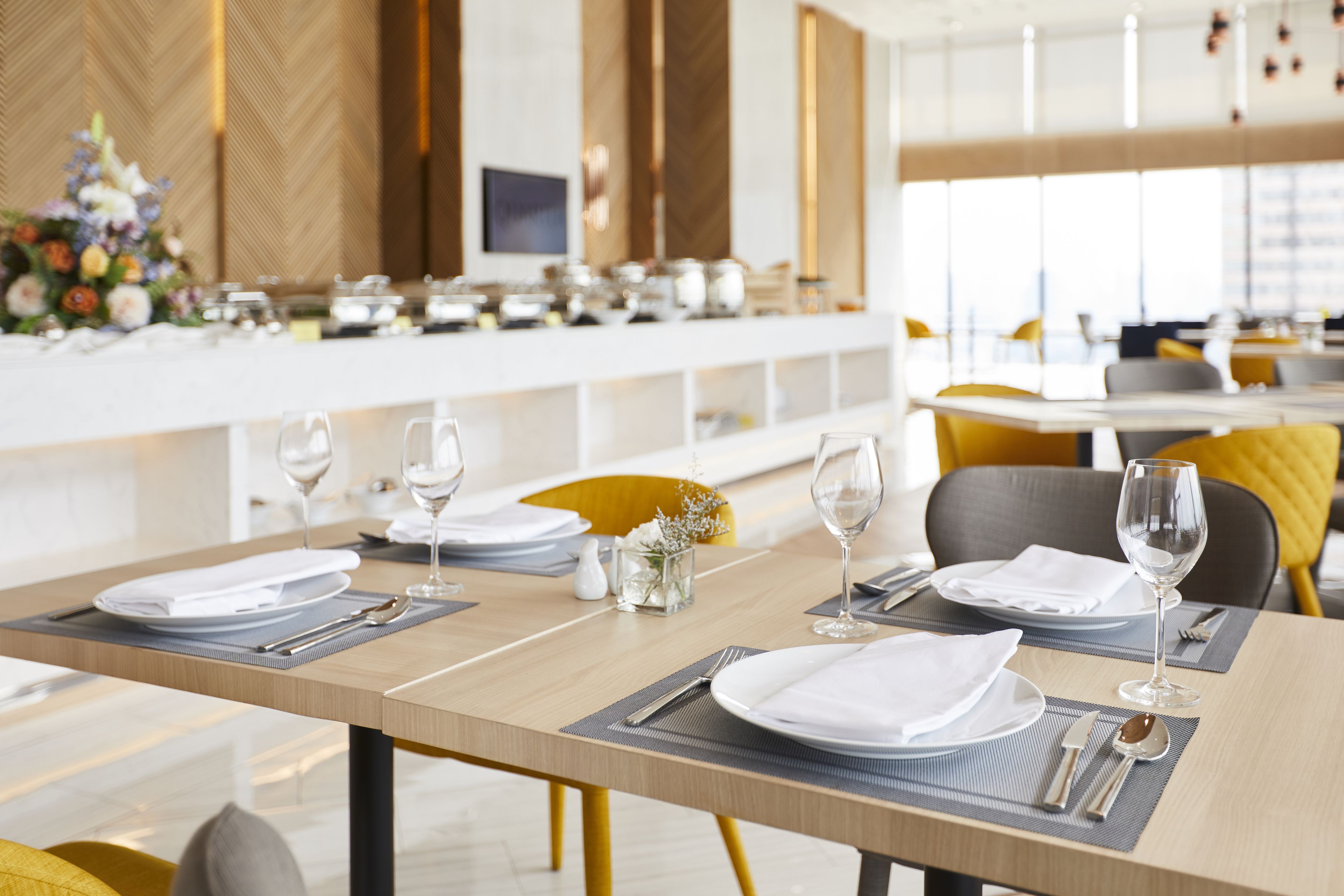 Un espace repas avec des tables dressées pour un repas, présentant un design moderne avec des tables en bois et des chaises jaunes.