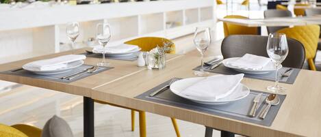 Un espace repas avec des tables dressées pour un repas, présentant un design moderne avec des tables en bois et des chaises jaunes.