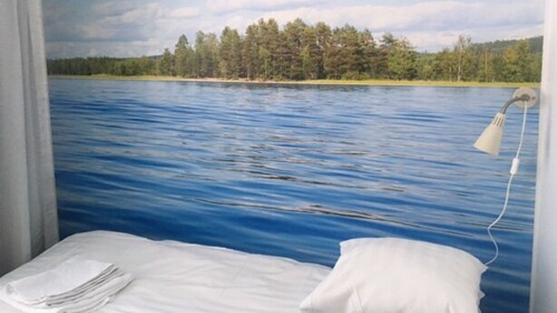 A room with a bed, a white pillow, and a wall mural of a lake with trees. - Place to Sleep Hotel Rauma (Rauma)