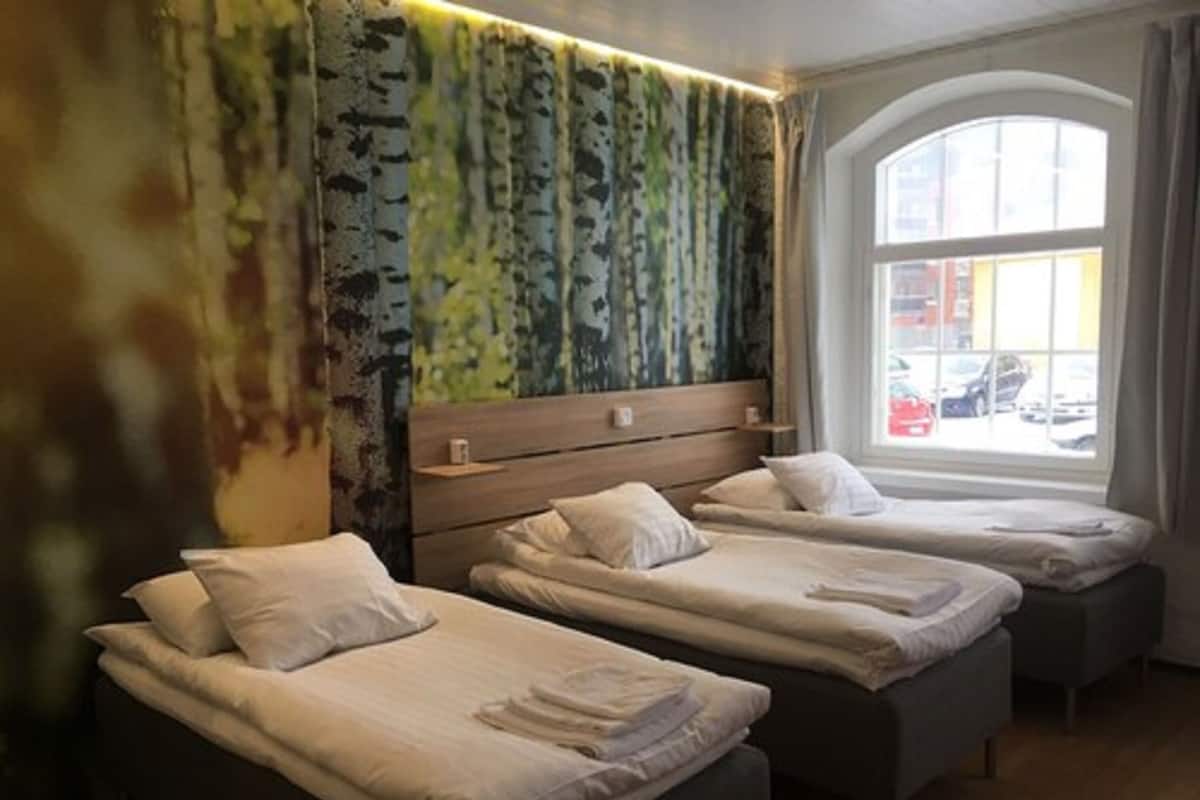 A hotel room with two single beds, a large window with a view of the street, and a unique green and blue patterned wall.
