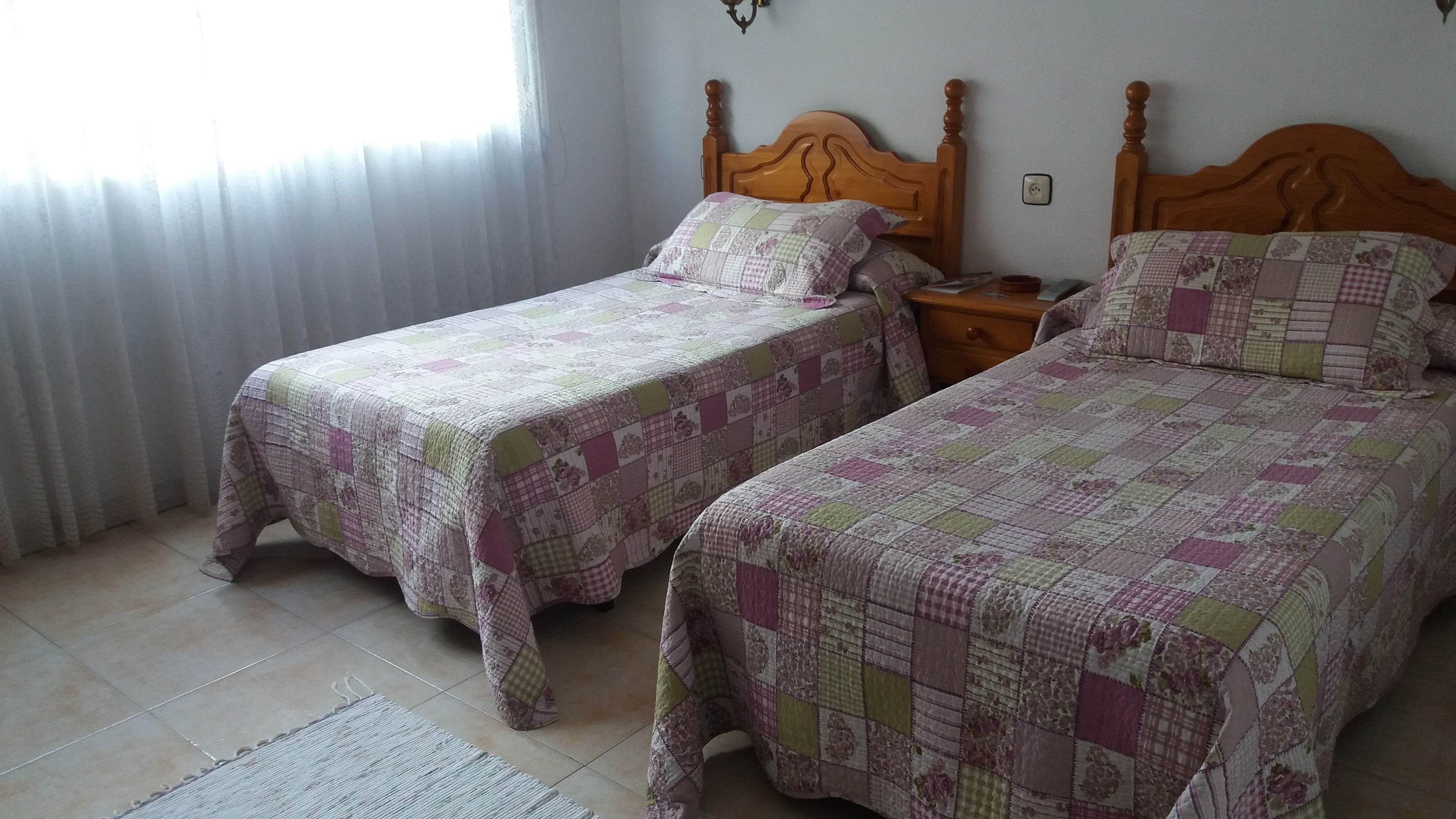 Two single beds with wooden headboards, a nightstand, and a window with curtains.