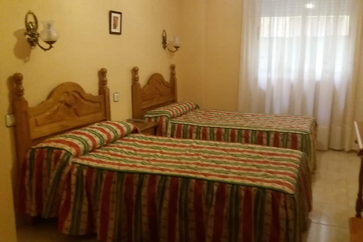 Ein Hotelzimmer mit zwei hölzernen Betten, belegt mit gestreifter Bettwäsche, einem Fernseher auf einem Holztisch und einem Fenster mit durchsichtigen Vorhängen.