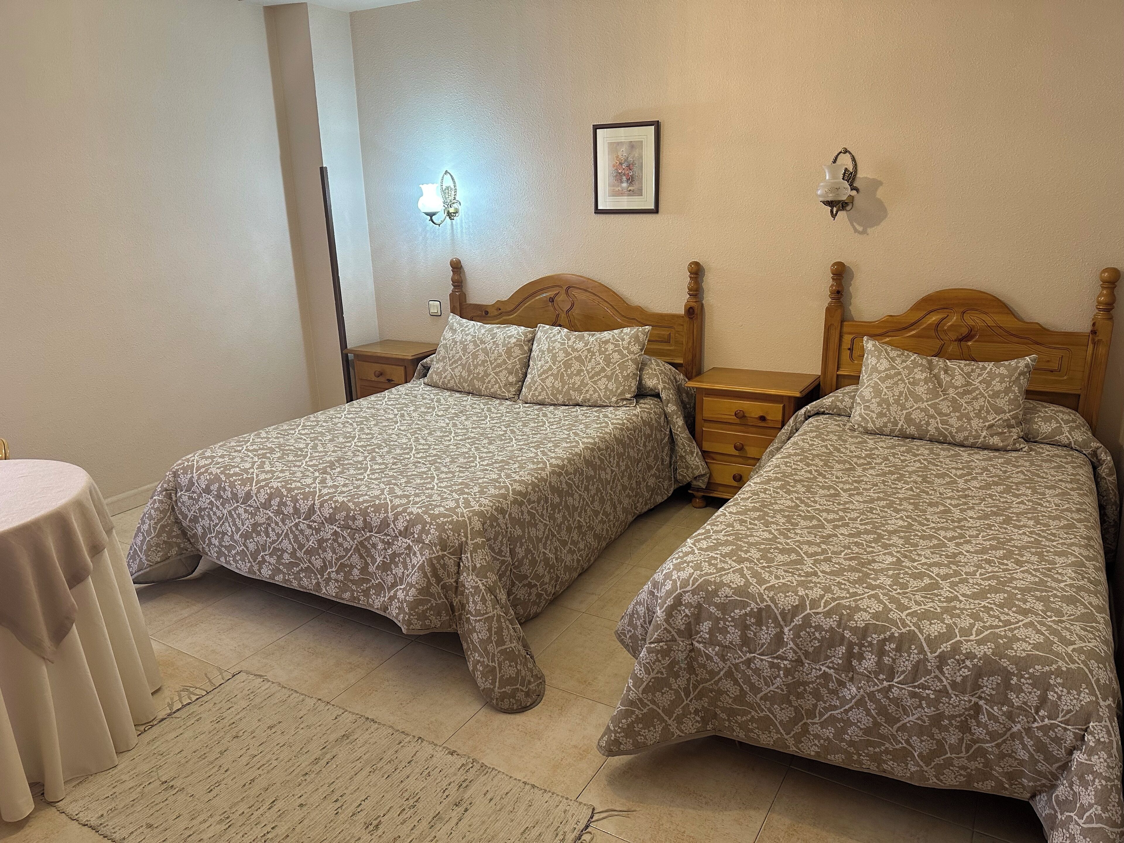 Una habitación con dos camas individuales, una mesita pequeña y una mesita de noche fijada a la pared.