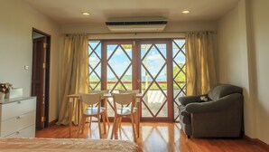 A room with a bed, a desk with chairs, a sofa, and a large window with curtains. - Phuripimarn Penthouse (Pak Chong)