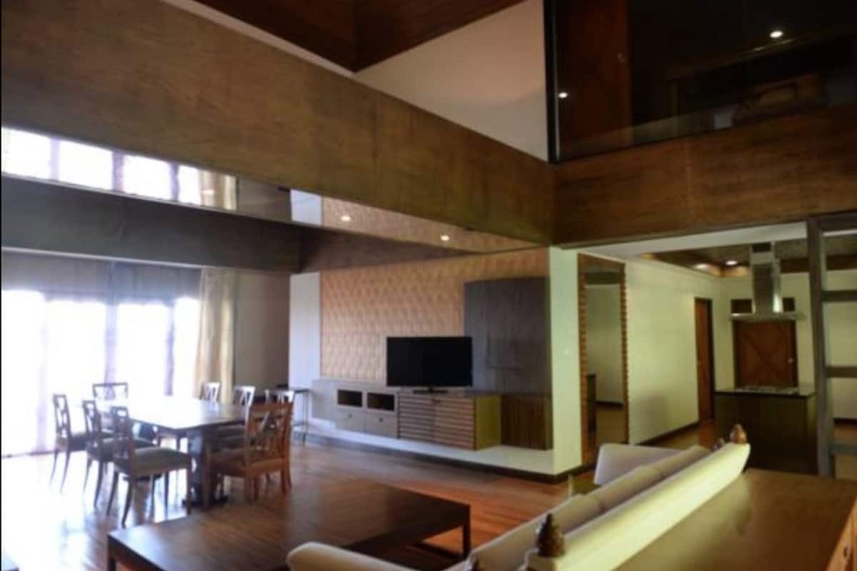 A spacious living area with a dining table, chairs, a sofa, and a flat-screen TV mounted on a wooden cabinet.
