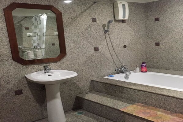 A bathroom with a white pedestal sink, a freestanding bathtub, and a mirror with a wooden frame.