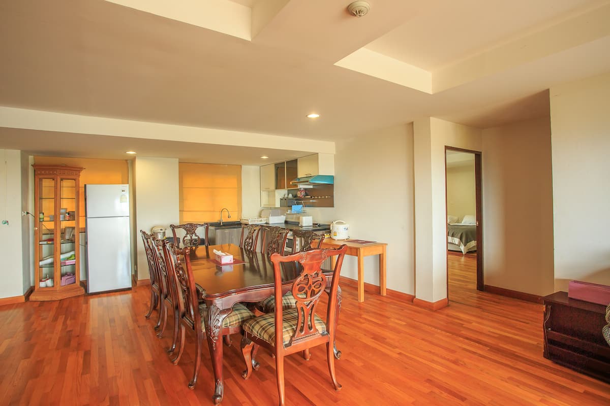 A spacious dining area with a wooden table and chairs, a kitchen in the background, and a hallway leading to a bedroom.