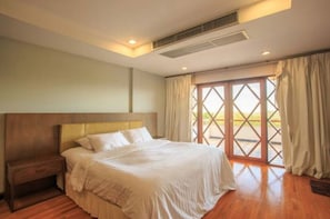 Une chambre à coucher avec un lit, une table de chevet, une fenêtre avec des rideaux et une vue sur la verdure à l’extérieur.