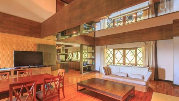 A spacious living area with a wooden floor, a large flat-screen TV, a sofa, and a dining table with chairs. - Phuripimarn Penthouse (Pak Chong)