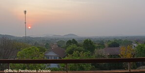 A sunset view from a balcony with a metal railing, overlooking a residential area with houses and greenery. - Phuripimarn Penthouse (Pak Chong)
