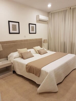 Quarto de hotel com cama, mesa de cabeceira, luminária e ar condicionado na parede.