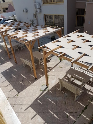Uma área externa com mesas e bancos de madeira, dispostos em um padrão de grade sobre um piso pavimentado.