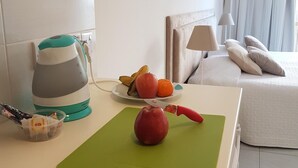 Une chambre d’hôtel équipée d’une kitchenette, d’un lit, d’une table de chevet avec des fruits et d’une lampe.