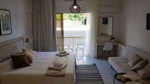 Une chambre d’hôtel avec un lit, un canapé, un bureau, une chaise, une petite table avec une tasse et un livre, et une vue sur l’extérieur.