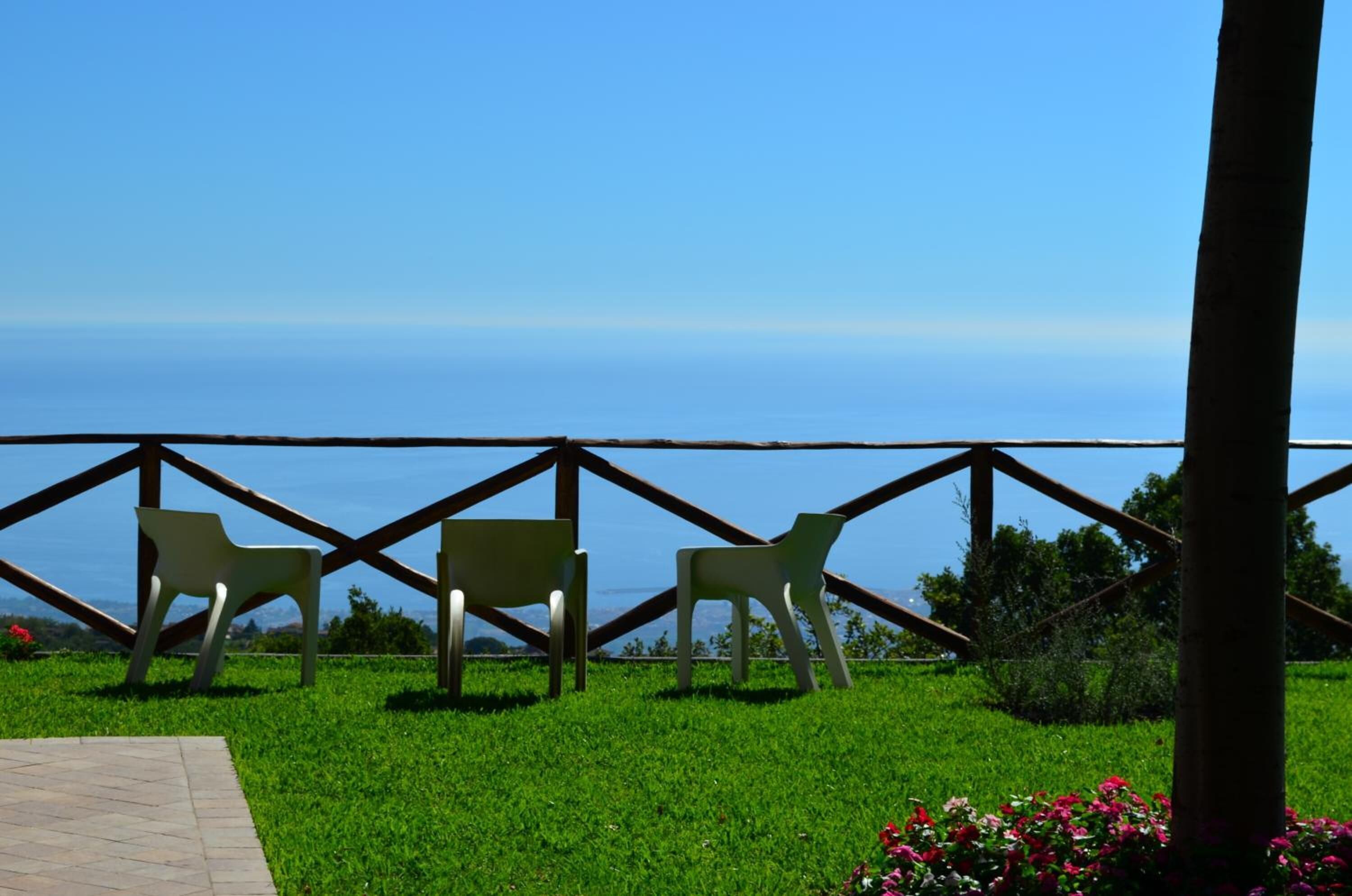 A grassy area with two white plastic chairs and a wooden fence overlooking a body of water.