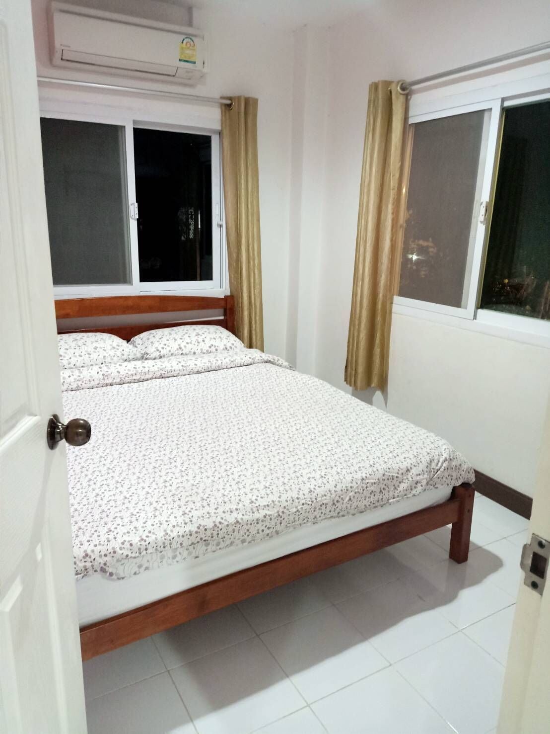 Un dormitorio con dos camas, una ventana con cortinas y un equipo de aire acondicionado.