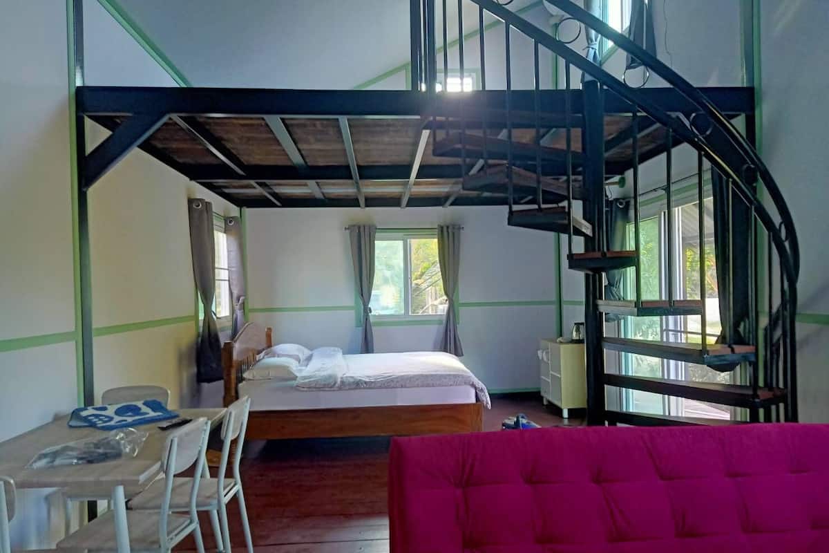 A bedroom with a bunk bed, a desk with chairs, a pink sofa, and a window with curtains.