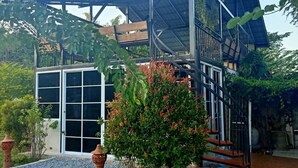 Una casa moderna con fachada de vidrio, un porche cubierto y un jardín con plantas en macetas.