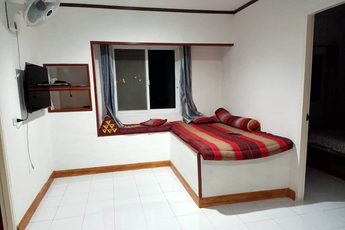 A bedroom with a bed, a window with curtains, a TV mounted on the wall, and a tiled floor.