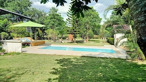 Una piscina rectangular con un área verde circundante, una terraza de madera y un paraguas verde.